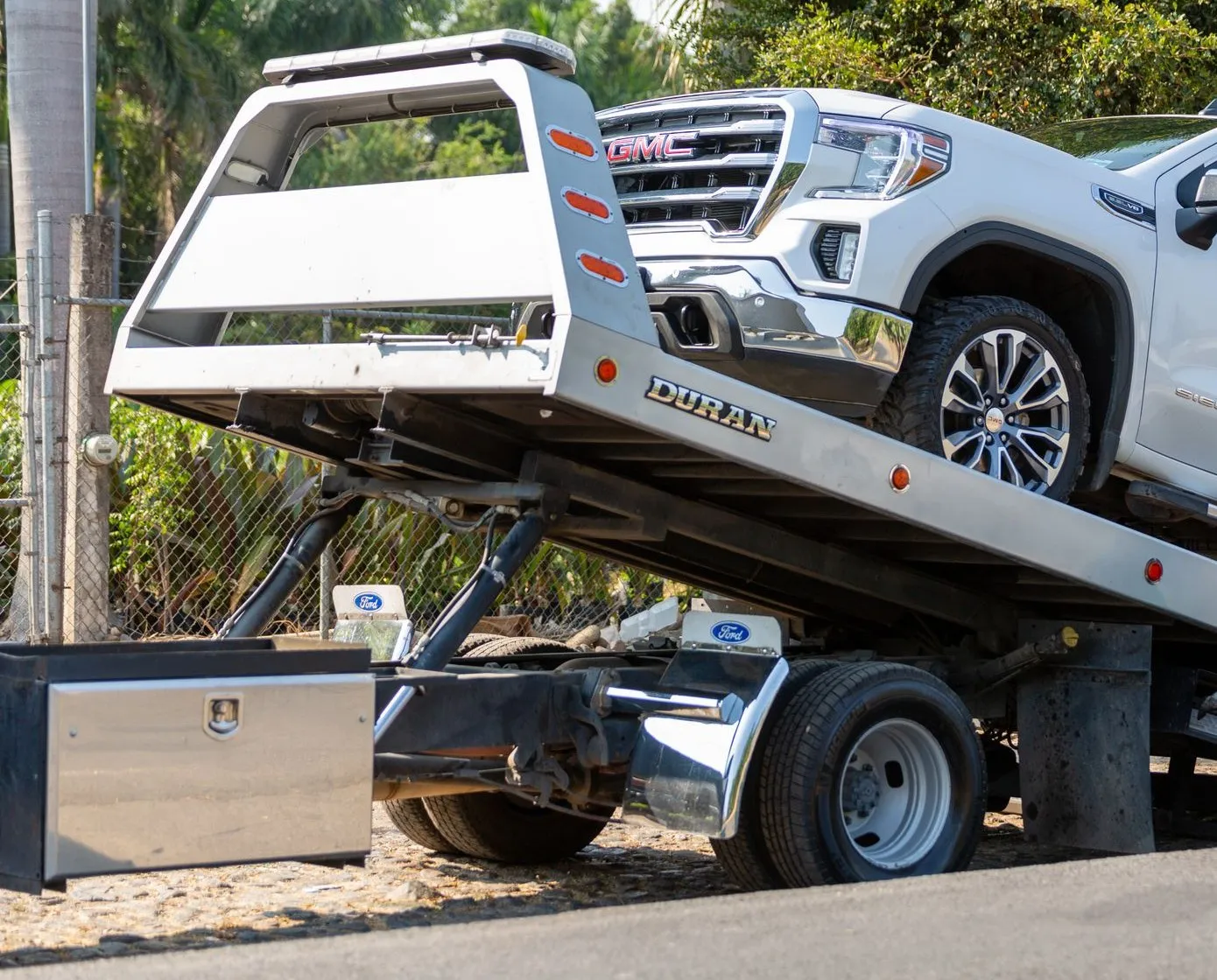 Tow truck with its bed tilted down, loading a white pickup